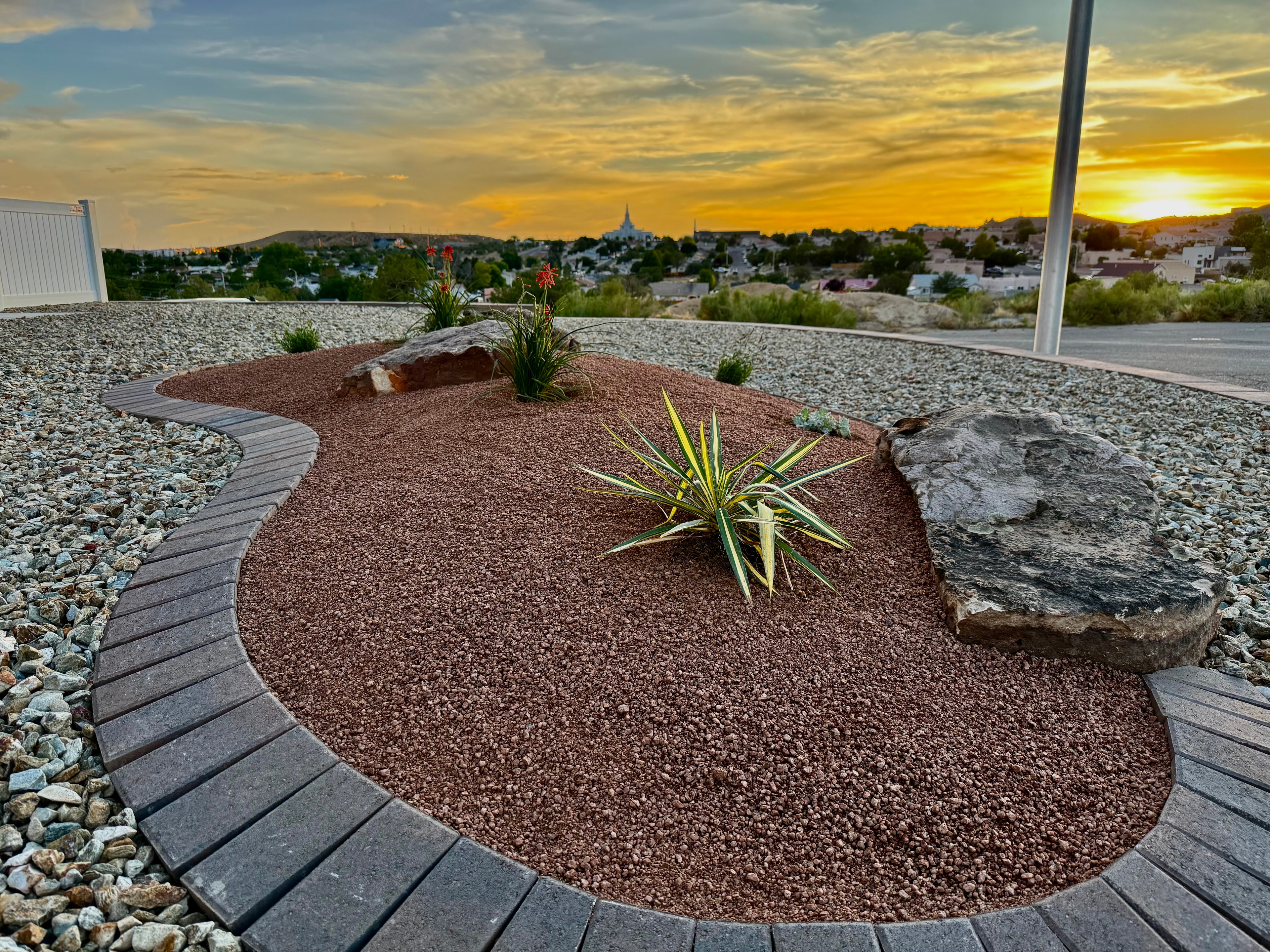Raised desert planting bed with paver border edging, moss rock, drought-tolerant plants, and decorative gravel at sunset in Farmington NM — High Desert NativeScapes