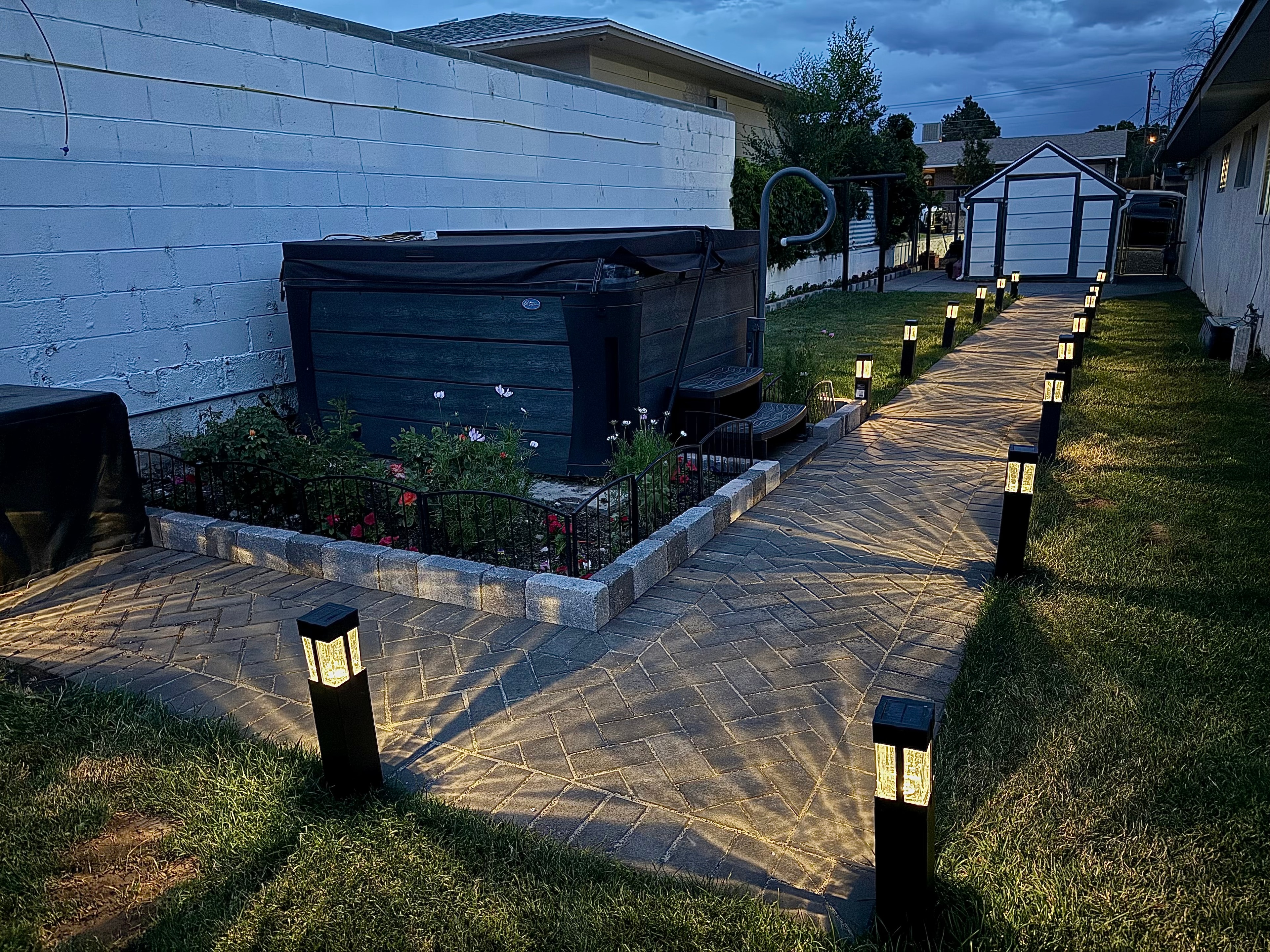 Charcoal herringbone paver pathway with bollard landscape lighting and grey-stone block hot tub garden bed border in Farmington NM — High Desert NativeScapes