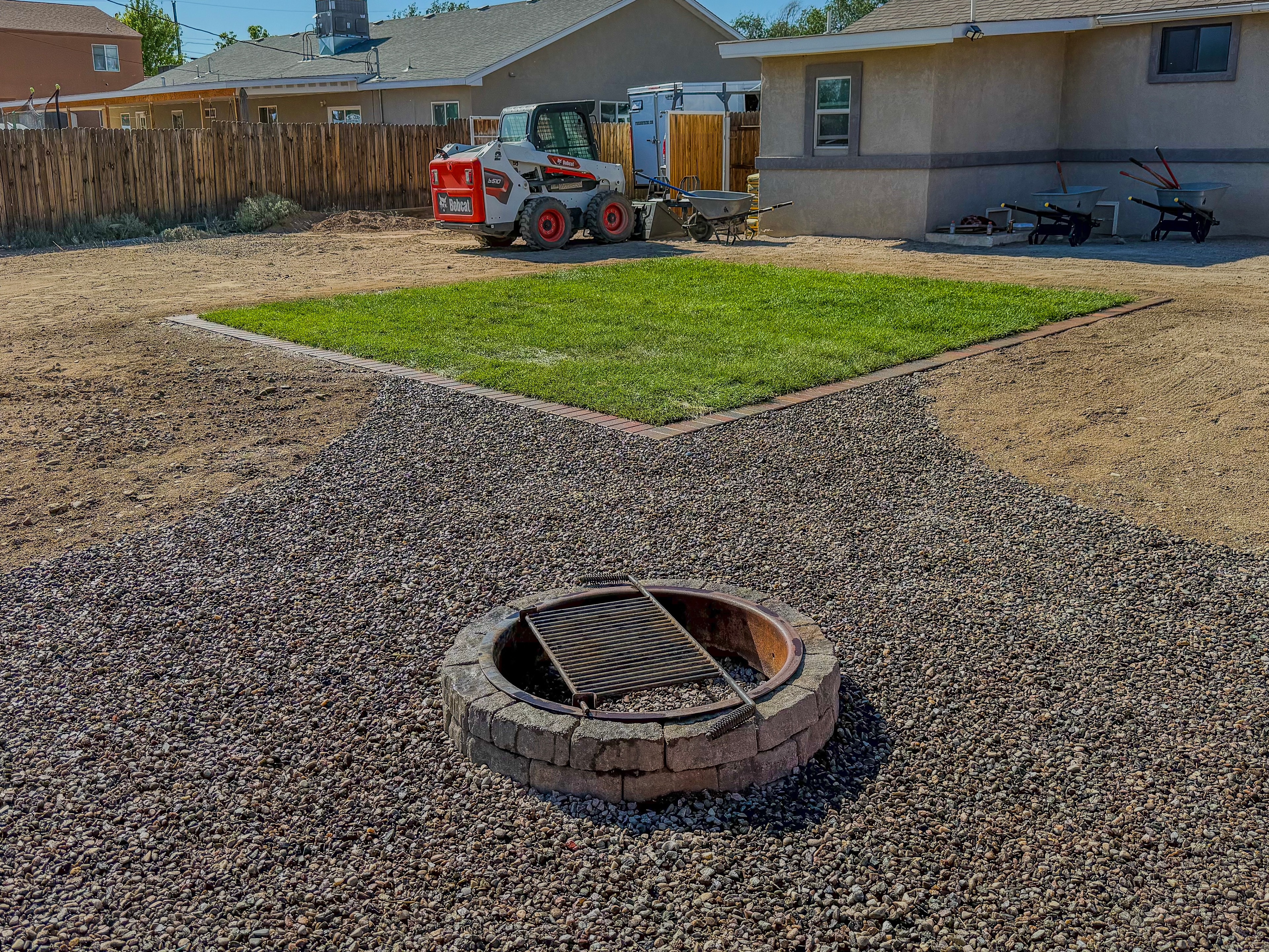 Backyard with sod lawn, paver border, gravel, and stone fire pit — High Desert NativeScapes, Farmington NM