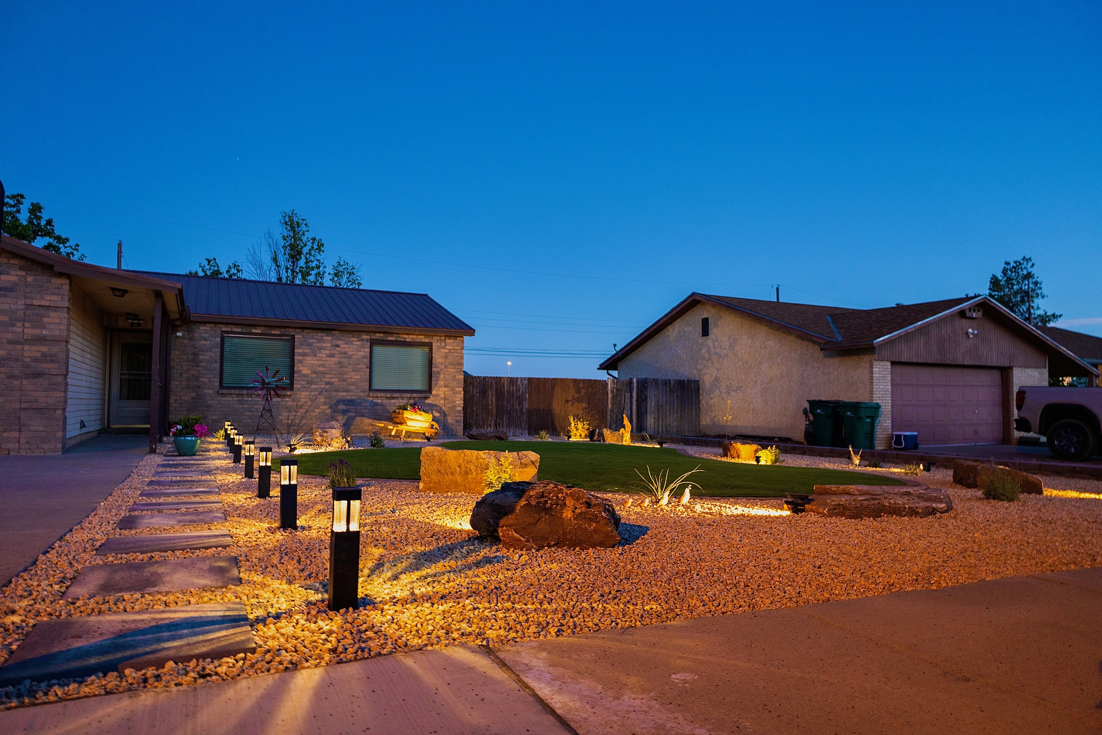 Artificial turf yard with paver stepper pathway along driveway, moss rock, and landscape lighting in Farmington NM — High Desert NativeScapes